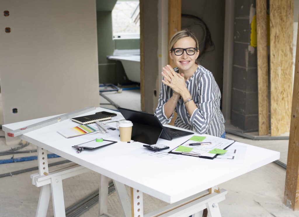 pretty young architect working on construction site in a loft and standing by a high table wearing glasses and grey and white striped top